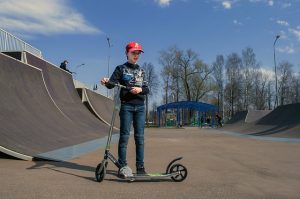 Child stands next to a vibrant scooter. The kid's hands firmly grip the handlebars of stunt scooter, ready to embark on an adventure.