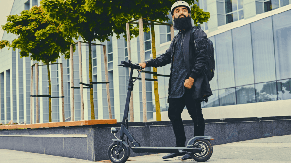 A man wearing black jacket holding his scooter. 