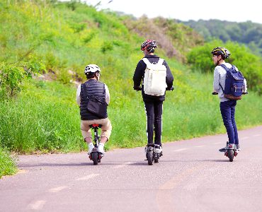 Three students with helmets ride scooters while going home from school. 