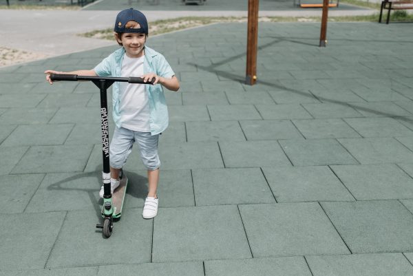 A happy toddler riding his scooter around the park.