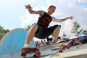 A man dressed in a black sleeveless shirt with his skateboard