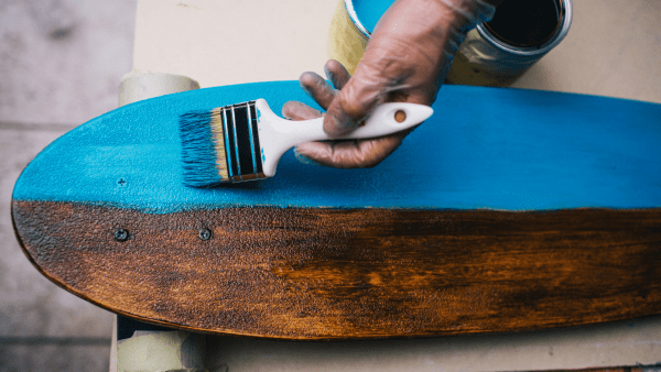 Skateboard - A hand painting the skateboard blue. It's half finished. Quality materials also contribute to both aesthetics and longevity.