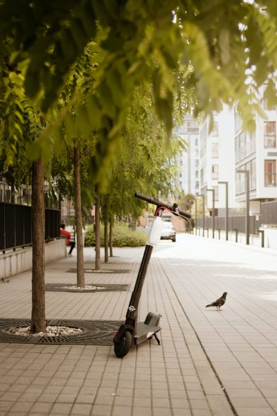 An electric scooter with a pretty high weight limit, parked in a street with only a few people. 