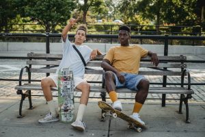 Two friends with skateboards sit outdoors. 