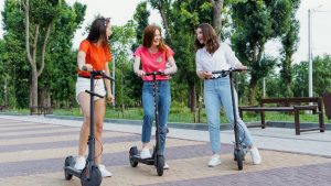 three ladies stand together, holding their scooters side by side in the park. They are clearly having a great time, laughing and engaged in a lively conversation. With their scooters at the ready, they are poised for a thrilling adventure in the park, making the most of their time together. A fun way to improve balance with a scooter.