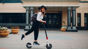 A woman in a white blouse and hat, joyfully riding her scooter with focused mind.