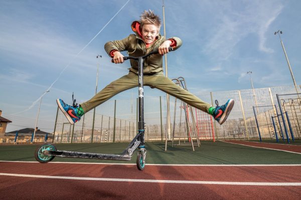 A young boy doing a jump trick on his kick scooter