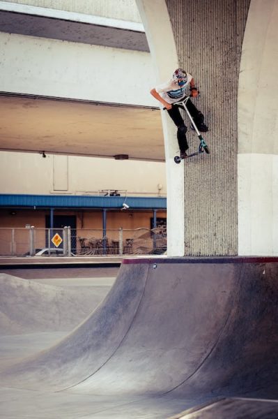 A man in a helmet doing scooter tricks on a ramp at a skate park