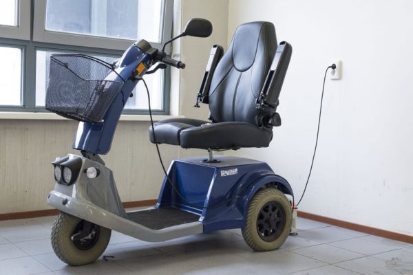 An electric scooter with three wheel is charging. 
