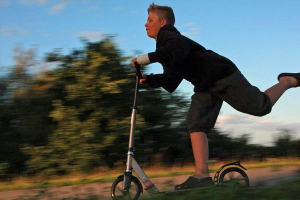 A boy wearing black sweater is riding his scooter.