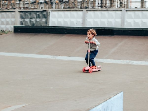  Infant on their pink three-wheeled scooter riding on a track.