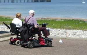 Two elderly people sit on a scooter. 