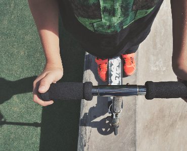 A person holding the scooter's handlebar while traveling outdoors. 