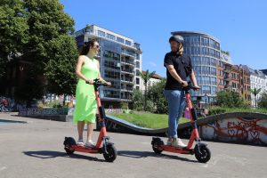 Two adults converse while riding their scooters.