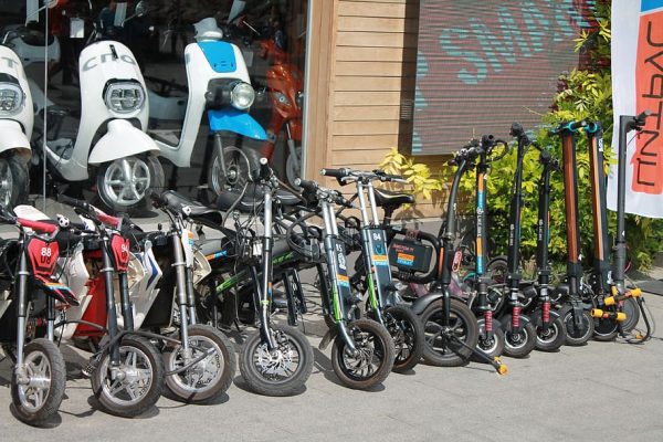 Different kinds of scooters are displayed inside and outside the store waiting for buyers. Some have big wheels and some are small.