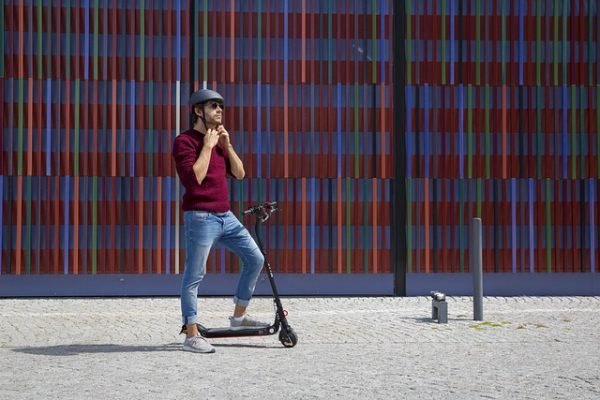 A man in a maroon shirt is wearing his helmet before riding his scooter.