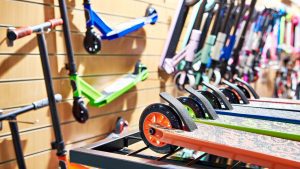 An array of colorful scooters with a variety of scooter decks displayed on a rack in a sports store, with the focus on the vibrant wheels and deck designs.