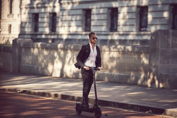A man wearing a suit while riding a scooter down the street