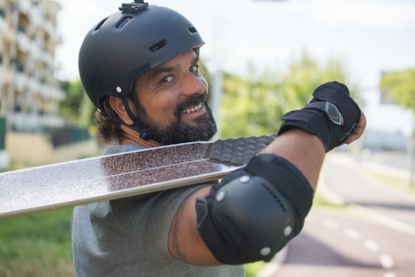 A man holding his board on his shoulder. He is also wearing protoctive equipment for his safety. 