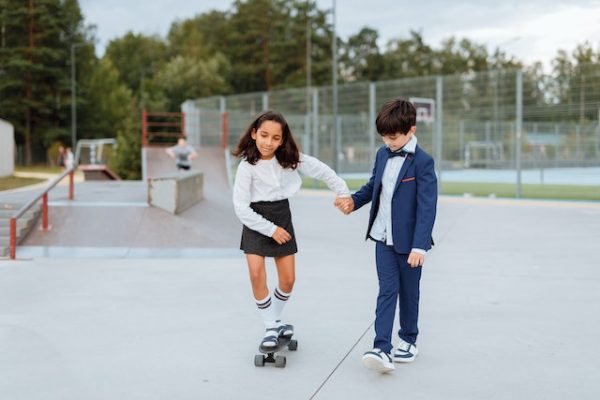 Two kids in a skate park teaching each other how to ride a skateboard. 