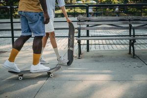 Two kids at a park, one teenager riding a skateboard with focused precision, and the other kids standing next to a bench, holding a skateboard, suggesting they are discussing skateboard or taking a break from skateboarding.