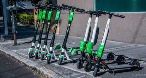 Several best green electric scooters parked on the sidewalk of the street.