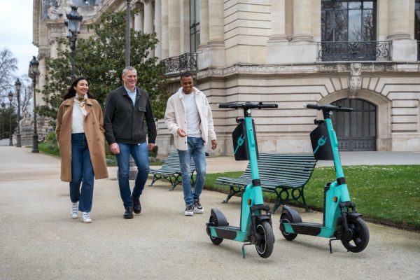 Three people walk towards their best two-wheeled electric vehicles while talking to each other. 
