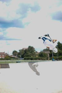  A person wearing white helmet does stunts while riding his scooter in the skatepark. 