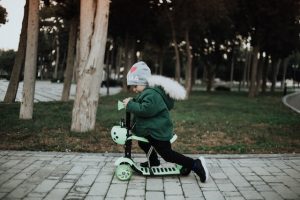 A kid rides a three-wheel scooter while playing in the park. 