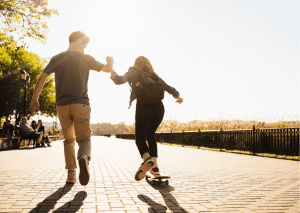 A gentleman teaching his friend to ride skateboards while enjoying their day at the skate park. 