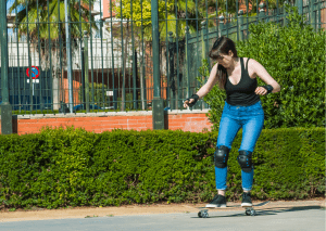 A woman with black sleeveless shirt and knee pads practices skateboarding confidently. 
