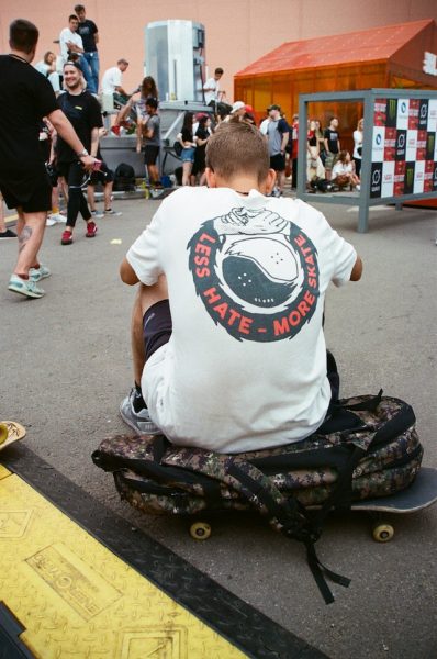 A man sits comfortably atop his skateboard bag in front of skaters after skateboarding session.