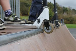  A boy's foot is positioned to a scooter with small wheels on a scooter ramp. Scooter wheels must be checked. The wheel and scooters are important for scooter wheel ride. 