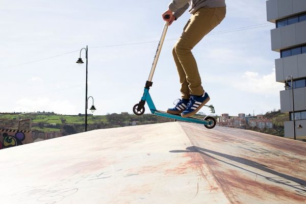 a boy riding small scooter wheels on a ramp with scooter trick.