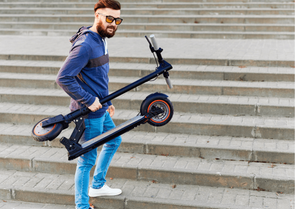 A bearded man with sunglasses is holding a foldable scooter. 