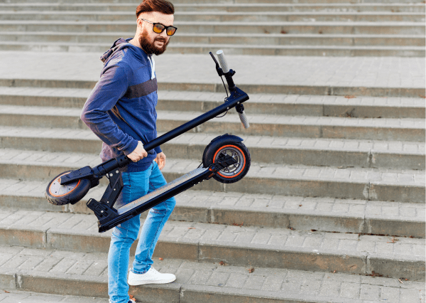 A bearded man with sunglasses is holding a foldable scooter.
