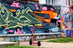 Electric vehicle parked in front of a wall with a very colorful graffiti.