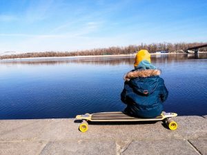 Kid sitting on skateboard, gazing out at the ocean. Best skateboards for kids.