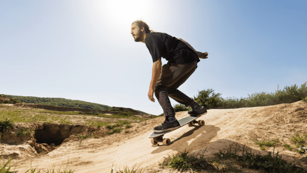 A man wearing a black shirt, & comfy pants, riding a skateboard. 