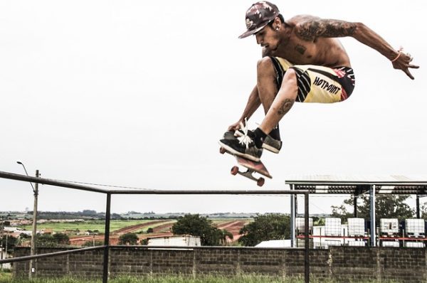 Importance of skateboarding training equipment - A shirtless tattooed man doing a skateboard trick in the air. He is lacking skateboarding training equipment.