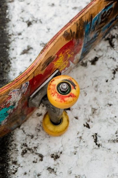 A board with yellow-orange wheels with a design on the body is lying down sideways on a pavement full of snow. 