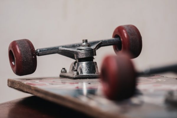 A shiny used board lying upside down on a floor with red wheels and is a bit used up