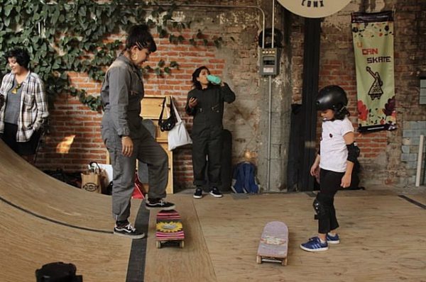  A teacher showing a kid skateboarding safety. Other people are lookign at them.