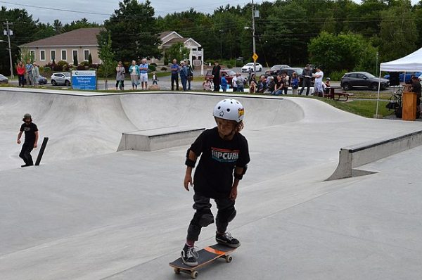 A kid is skateboarding with helmet for safety while other kids are watching.