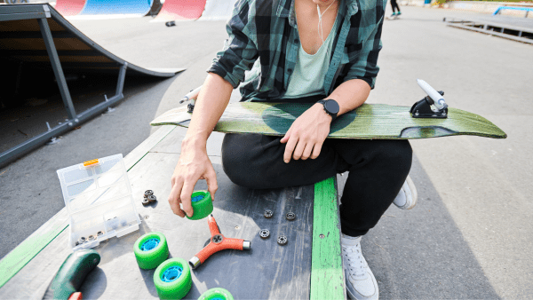 A skateboarder sitting on a bench and repairing a board. 