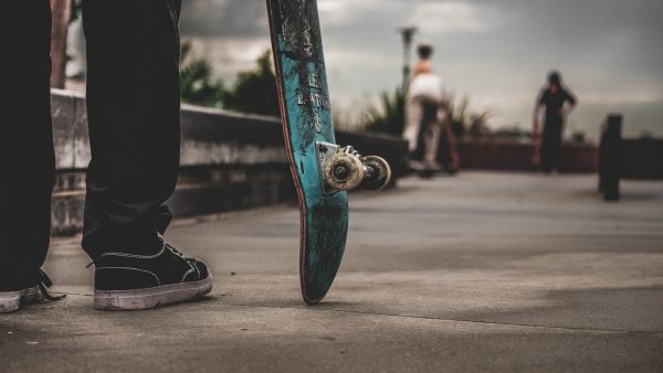 A man in black shoes is holding his skateboard while going to a skate park.