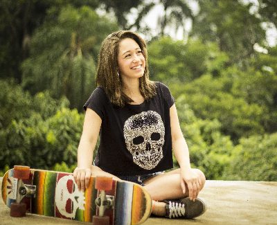 A female sits on the yard and smiles while wearing female skateboard attire designed with an emphasis on both style and functionality.