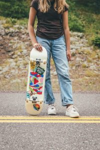 A person holds a cruiser skateboard while standing. 