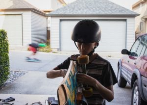 A young man wearing a helmet assembles the wheels of his cruiser skateboard. 