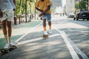 Two adults are skateboarding on the sidewalk. 